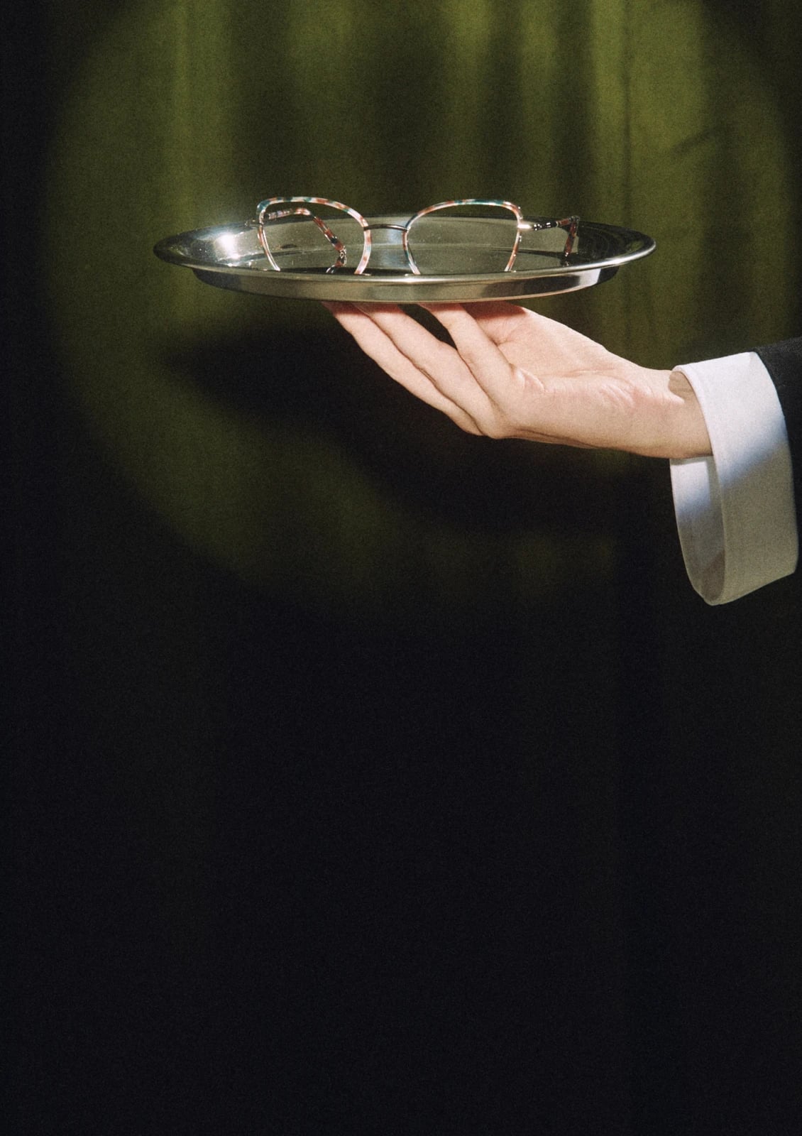 Mano que ofrece unas gafas en una bandeja de plata, colección AW26